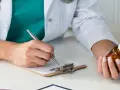 Lekarz rodzinny pisze receptę na leki na nerwicę, trzymając w dłoni buteleczkę z lekami.