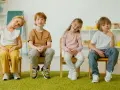 Cztery dzieci siedzą na krzesłach. Czy ADHD to choroba psychiczna? Dzieci wyglądają na zamyślone, jakby zastanawiały się nad trudnym pytaniem.