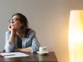 Kobieta w okularach zamyślona przy biurku, zastanawia się nad neurotycznością. Obok filiżanka kawy i lampa.
