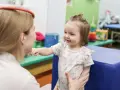 Terapia sensoryczna dla dzieci: uśmiechnięta dziewczynka w gabinecie terapeutycznym, wspierana przez specjalistkę.