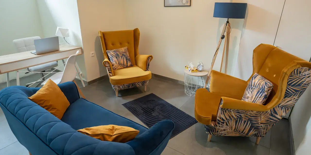 Nowoczesny gabinet psychologiczny z żółtymi fotelami, niebieską kanapą i biurkiem.