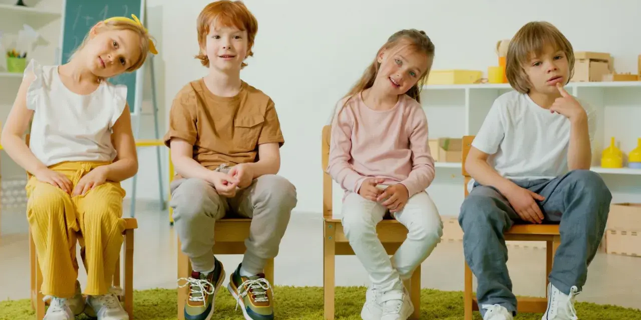 Cztery dzieci siedzą na krzesłach. Czy ADHD to choroba psychiczna? Dzieci wyglądają na zamyślone, jakby zastanawiały się nad trudnym pytaniem.