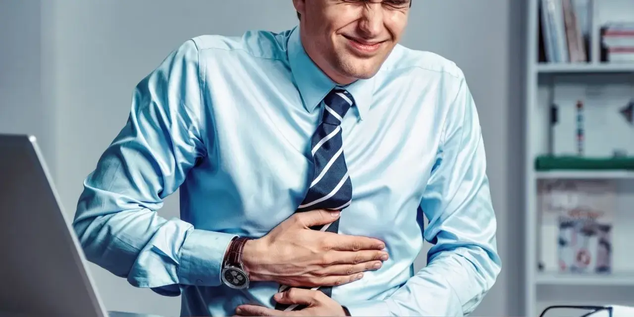 Mężczyzna w biurze cierpi na bóle brzucha, które mogą być objawem dyspepsji nerwicowej.