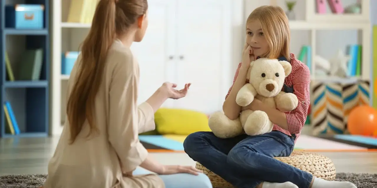 Przykładowa rozmowa z psychologiem. Dziewczynka z misiem słucha uważnie terapeuty.