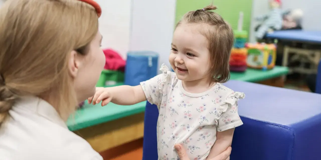 Terapia sensoryczna dla dzieci: uśmiechnięta dziewczynka w gabinecie terapeutycznym, wspierana przez specjalistkę.