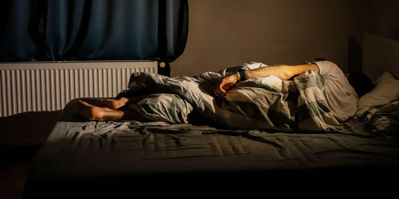 Osoba śpi pod kołdrą, z nogami wystającymi spod niej. Może to być sposób na zaśnięcie w 2 minuty.