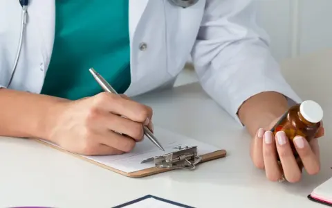 Lekarz rodzinny pisze receptę na leki na nerwicę, trzymając w dłoni buteleczkę z lekami.