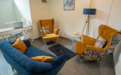Nowoczesny gabinet psychologiczny z żółtymi fotelami, niebieską kanapą i biurkiem.