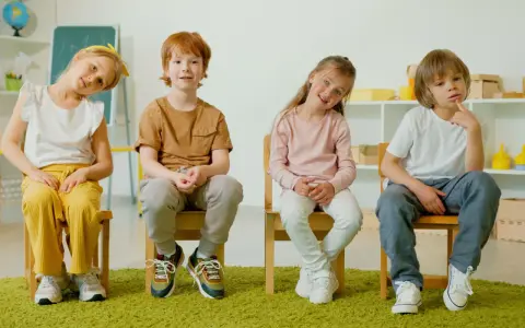 Cztery dzieci siedzą na krzesłach. Czy ADHD to choroba psychiczna? Dzieci wyglądają na zamyślone, jakby zastanawiały się nad trudnym pytaniem.