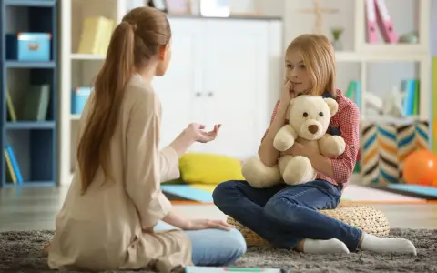 Przykładowa rozmowa z psychologiem. Dziewczynka z misiem słucha uważnie terapeuty.
