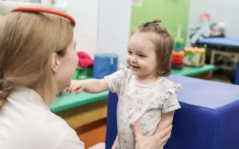 Terapia sensoryczna dla dzieci: uśmiechnięta dziewczynka w gabinecie terapeutycznym, wspierana przez specjalistkę.