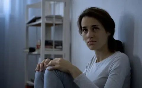 Zmartwiona kobieta siedzi przy ścianie. Jak zmusić schizofrenika do leczenia? Potrzebna jest empatia i wsparcie.