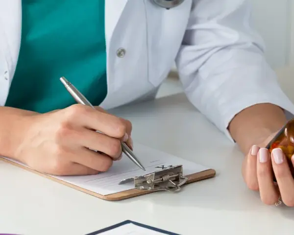 Lekarz rodzinny pisze receptę na leki na nerwicę, trzymając w dłoni buteleczkę z lekami.