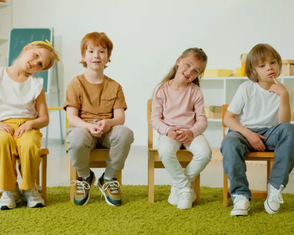 Cztery dzieci siedzą na krzesłach. Czy ADHD to choroba psychiczna? Dzieci wyglądają na zamyślone, jakby zastanawiały się nad trudnym pytaniem.