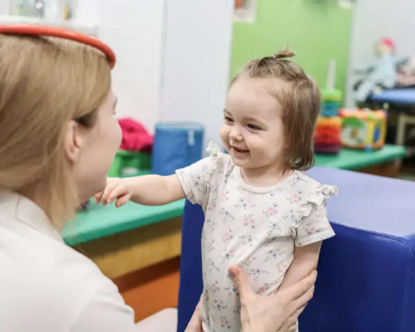 Terapia sensoryczna dla dzieci: uśmiechnięta dziewczynka w gabinecie terapeutycznym, wspierana przez specjalistkę.