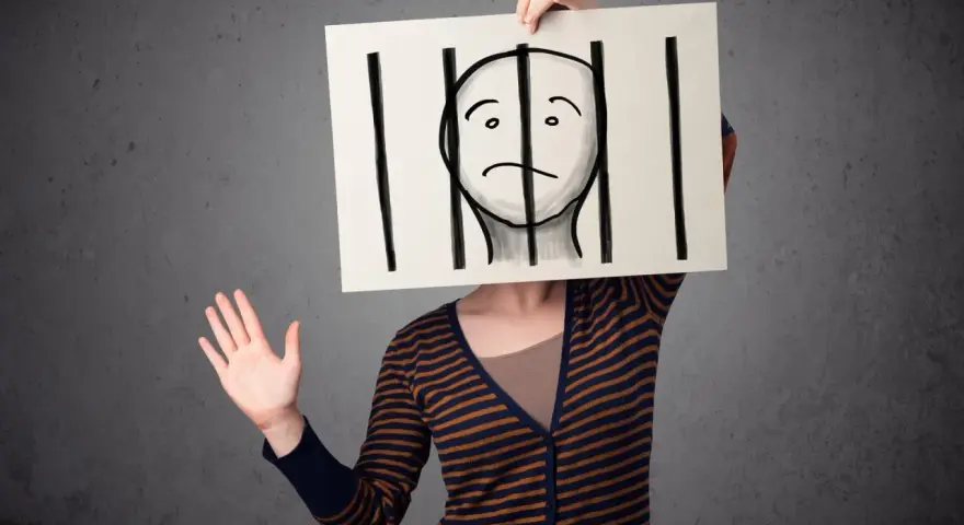 Osoba trzyma tabliczkę z rysunkiem twarzy za kratami. Czy to paranoik, który czuje się uwięziony?