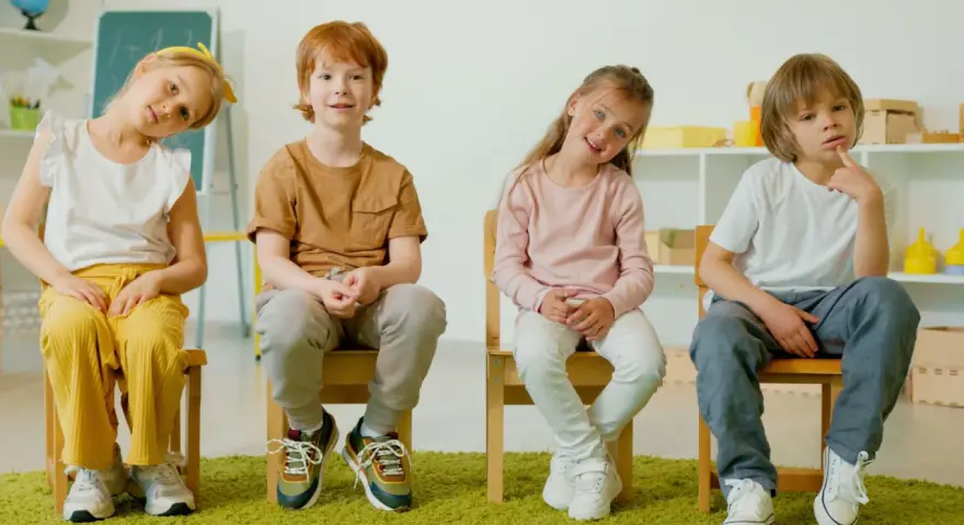 Cztery dzieci siedzą na krzesłach. Czy ADHD to choroba psychiczna? Dzieci wyglądają na zamyślone, jakby zastanawiały się nad trudnym pytaniem.