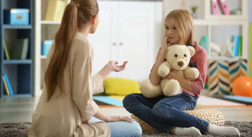 Przykładowa rozmowa z psychologiem. Dziewczynka z misiem słucha uważnie terapeuty.