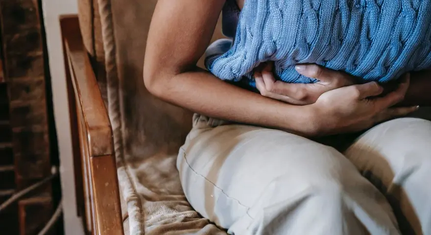 Osoba siedząca na krześle trzyma się za brzuch. Czy to objaw emetofobii?