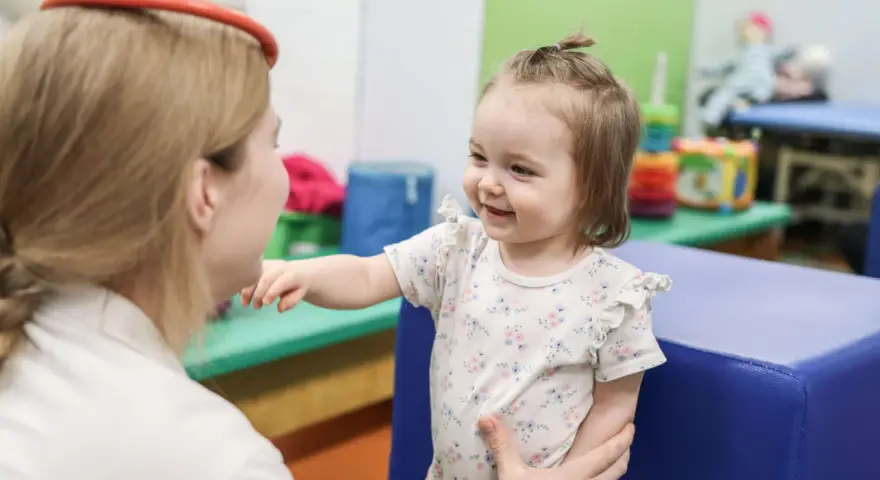 Terapia sensoryczna dla dzieci: uśmiechnięta dziewczynka w gabinecie terapeutycznym, wspierana przez specjalistkę.