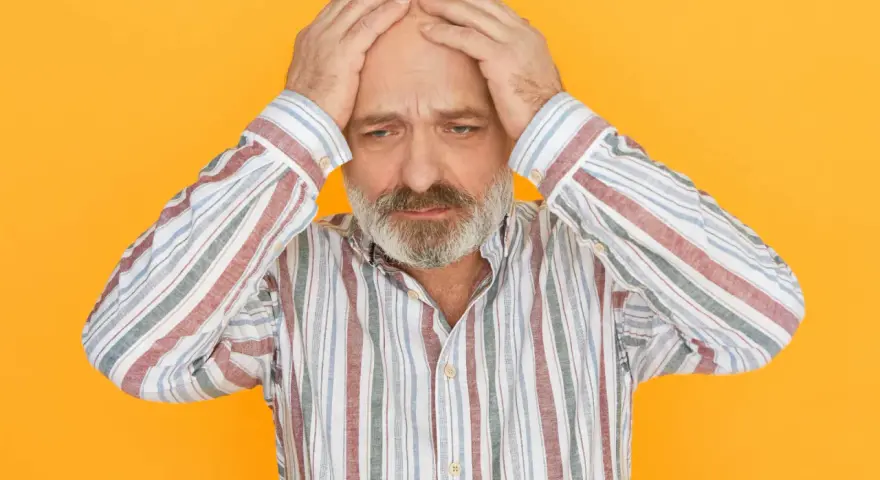 Mężczyzna w paski z rękami na głowie, smutny wyraz twarzy, na pomarańczowym tle.