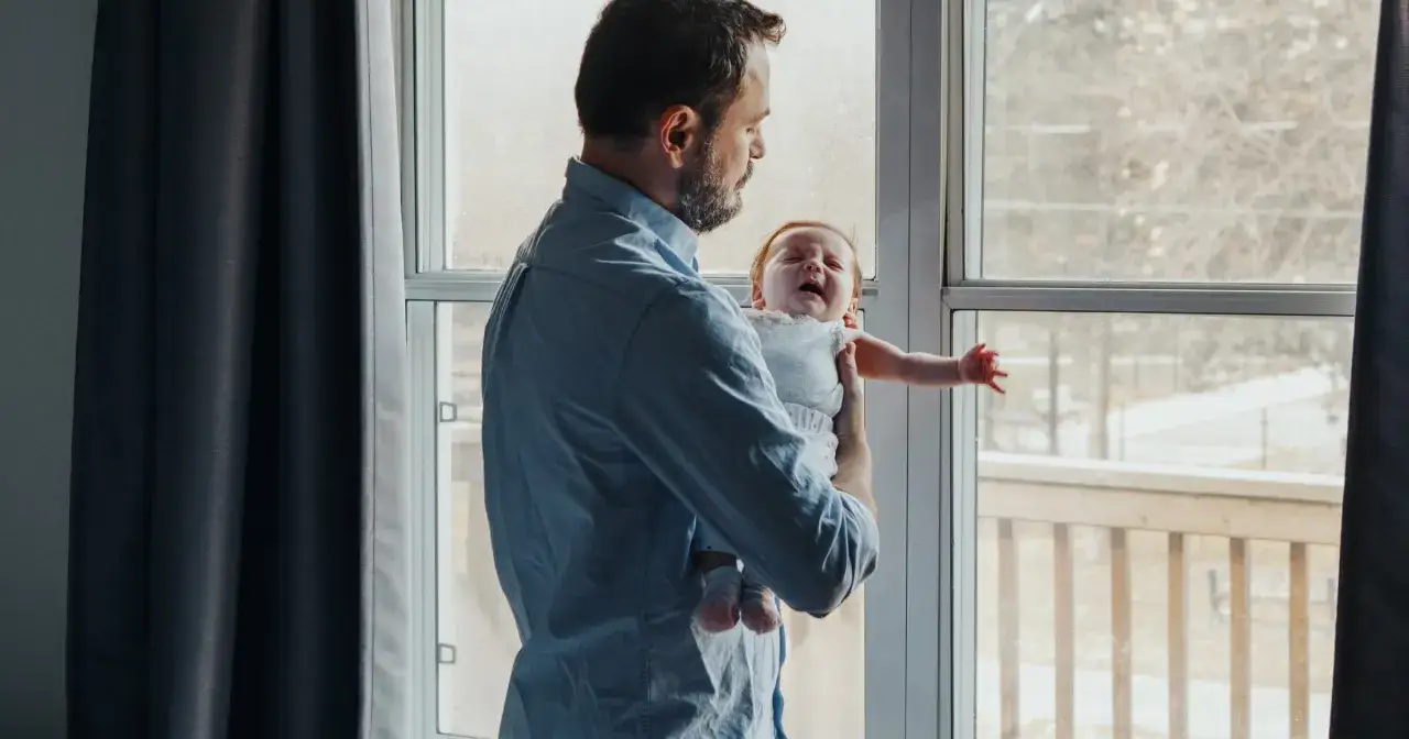 Ojciec trzyma płaczące dziecko przy oknie. Czy to objawy daddy issues?