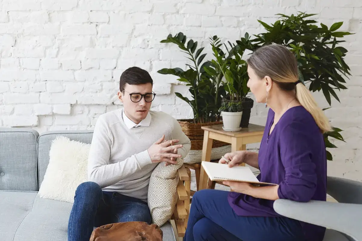 Mężczyzna w okularach rozmawia z kobietą, która notuje. To może być sesja, gdzie psycholog i psychoterapeuta różnice są kluczowe.