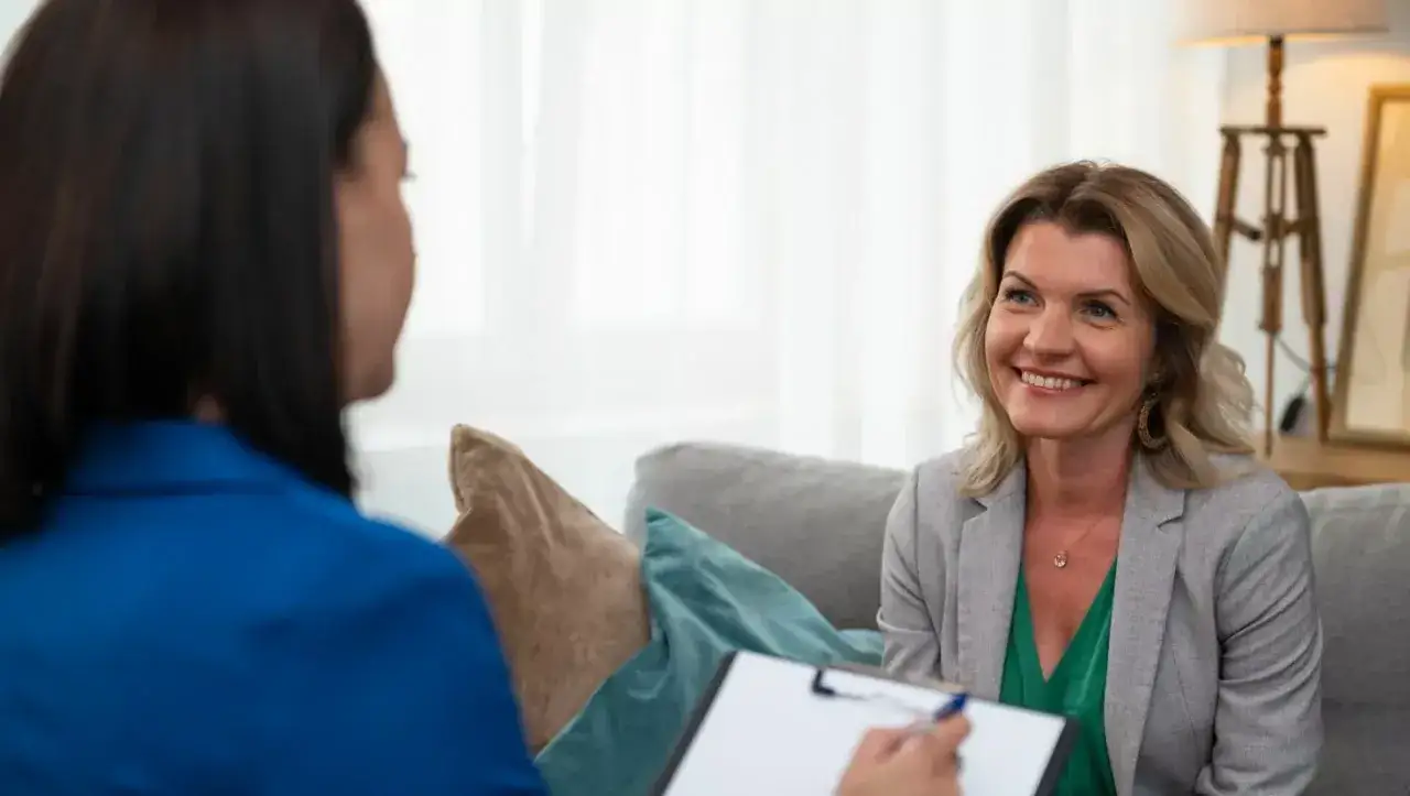 Uśmiechnięta kobieta podczas przykładowej rozmowy z psychologiem. Terapeuta notuje na kartce.
