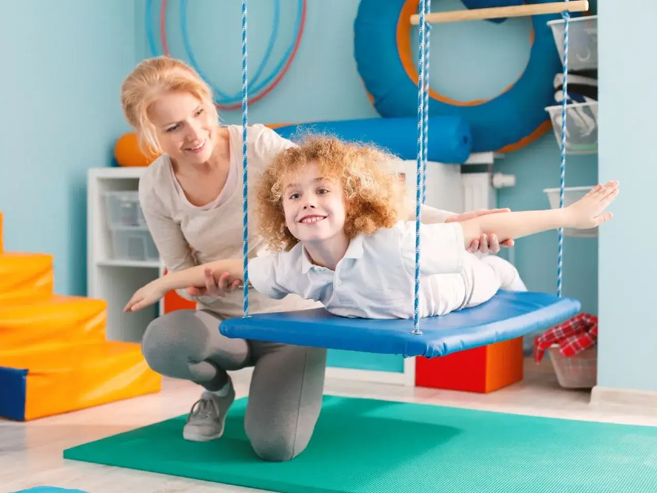 Terapia integracji sensorycznej: dziecko na huśtawce z terapeutką, ćwiczenia pomagające jak leczyc zaburzenia sensoryczne.